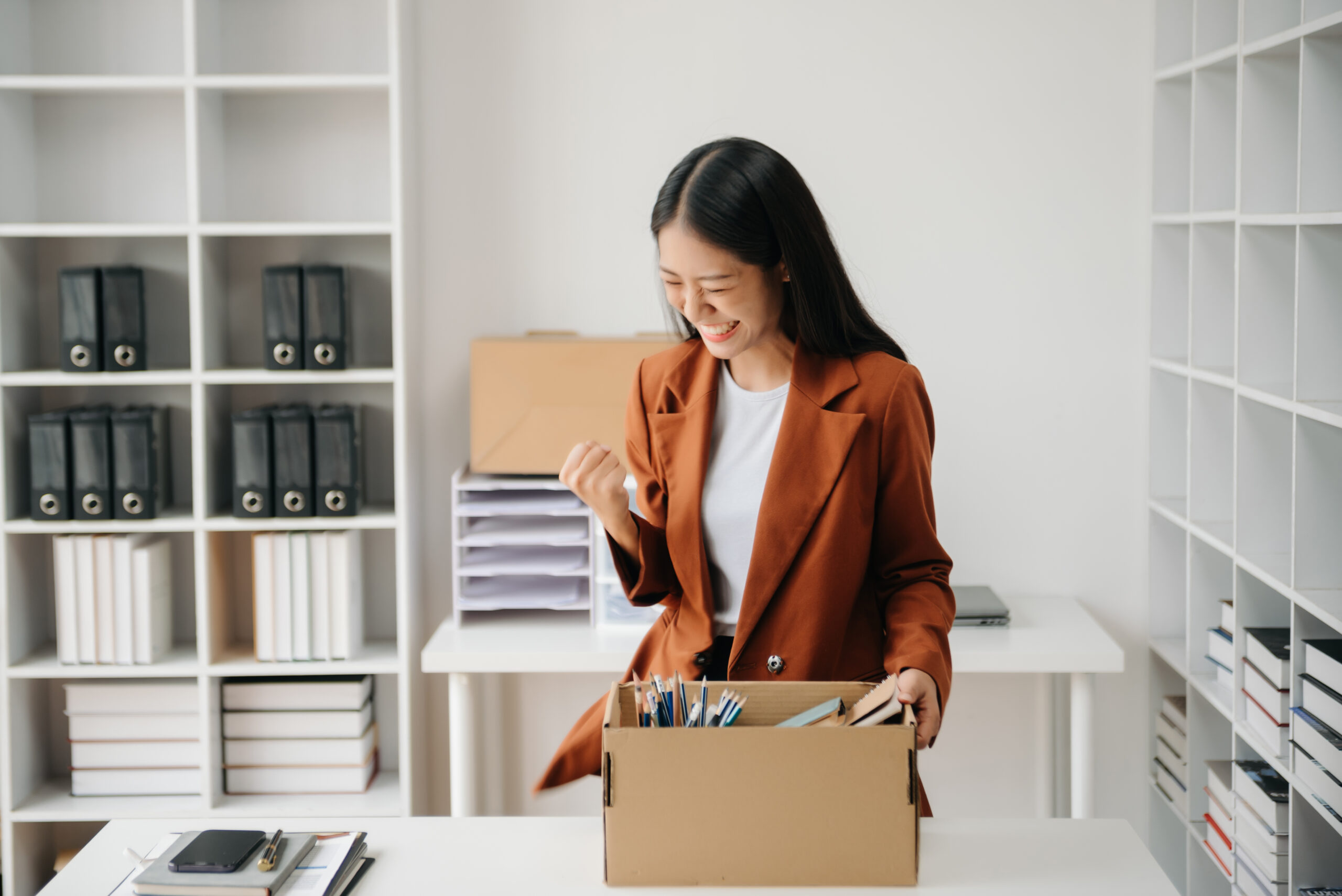 Happy and excited young beautiful Asian woman office worker celebrating her resignation, carrying her personal stuff. leaving job, changing or company.